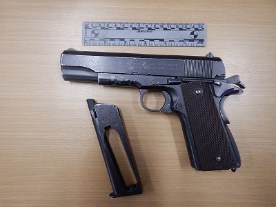 Photo d’un pistolet à plombs noir en métal avec une crosse brune et un chargeur éjecté sous une règle grise aux fins de perspective.