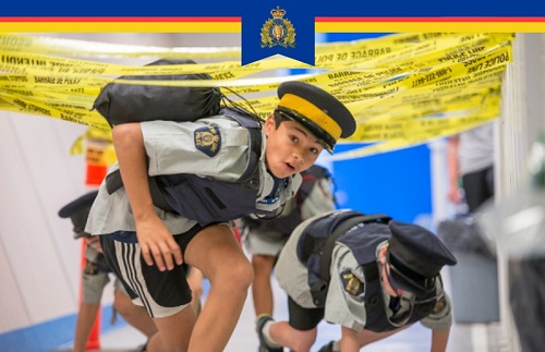 Youth wearing RCMP short sleeve shirt and RCMP forge cap crawling through obstacle course
