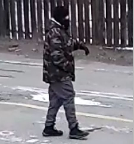 Homme, trapu, petit, vêtu d’une veste de camouflage et d’un masque noir