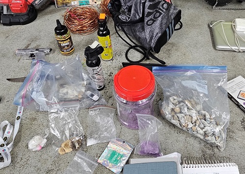 Seized items laid on the ground including suspected drugs in plastic bags, bear spray, bb gun and ammo